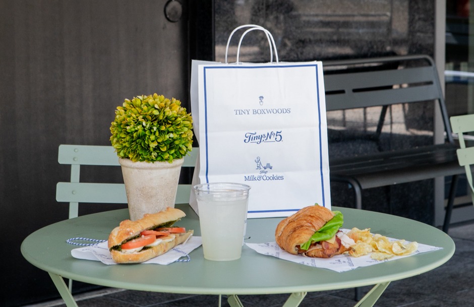 Lunch bistro table with to-go bag and sandwiches, chips, and drink